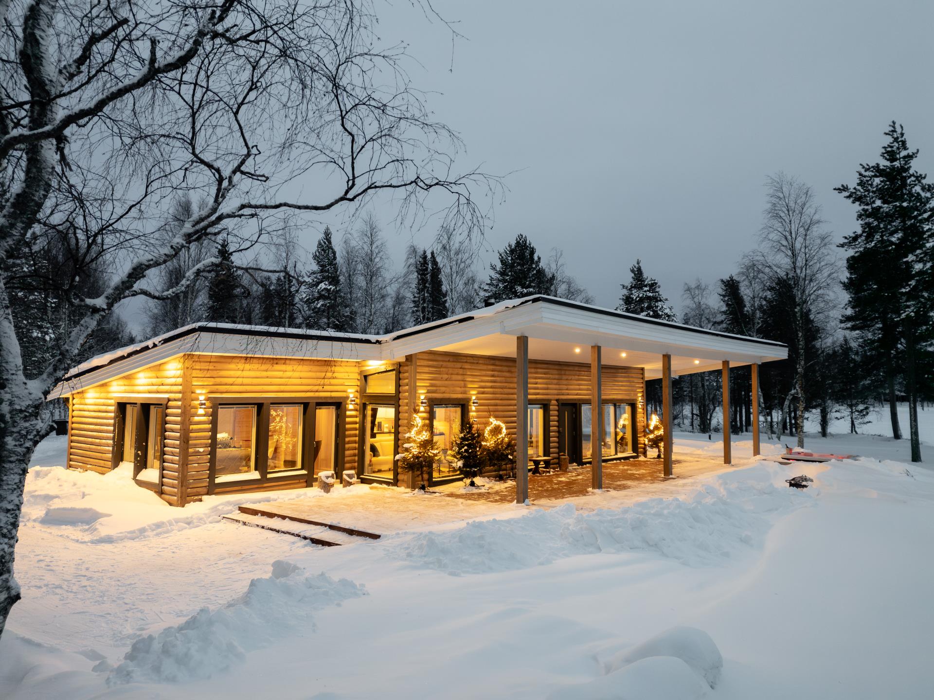 a house with lights on it in the wintertime in snowy nature.