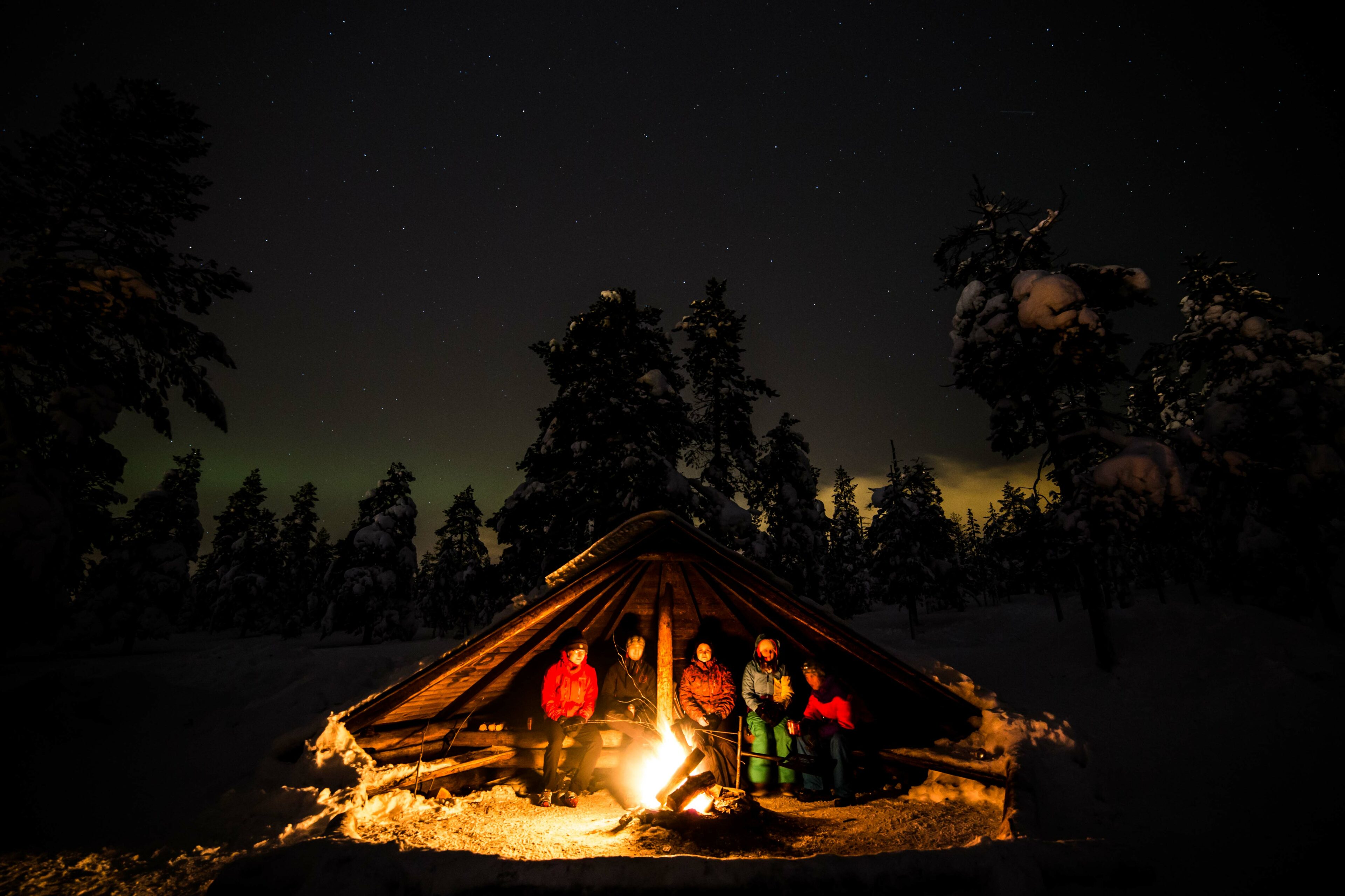 People sitting in a lean-to with a fire during a Northern Lights -tour.