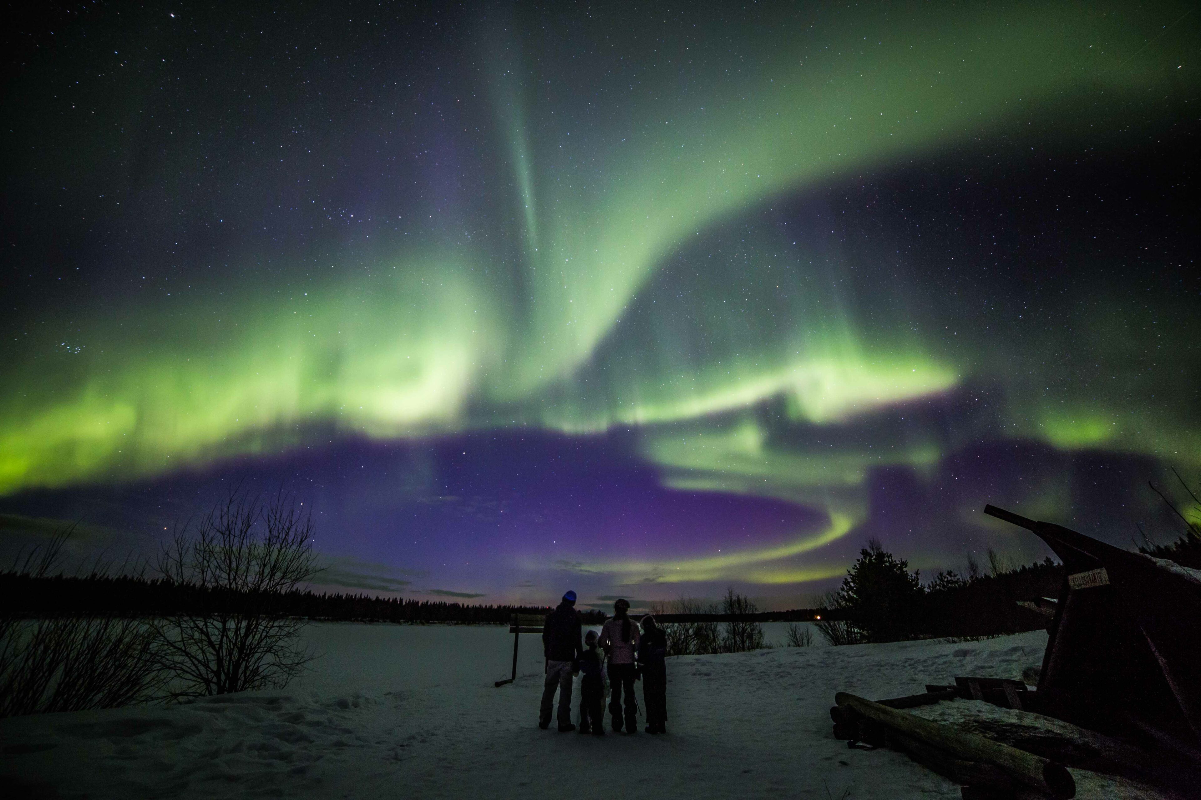 Family under green Northern Lights in Rovaniemi, Lapland, Finland.