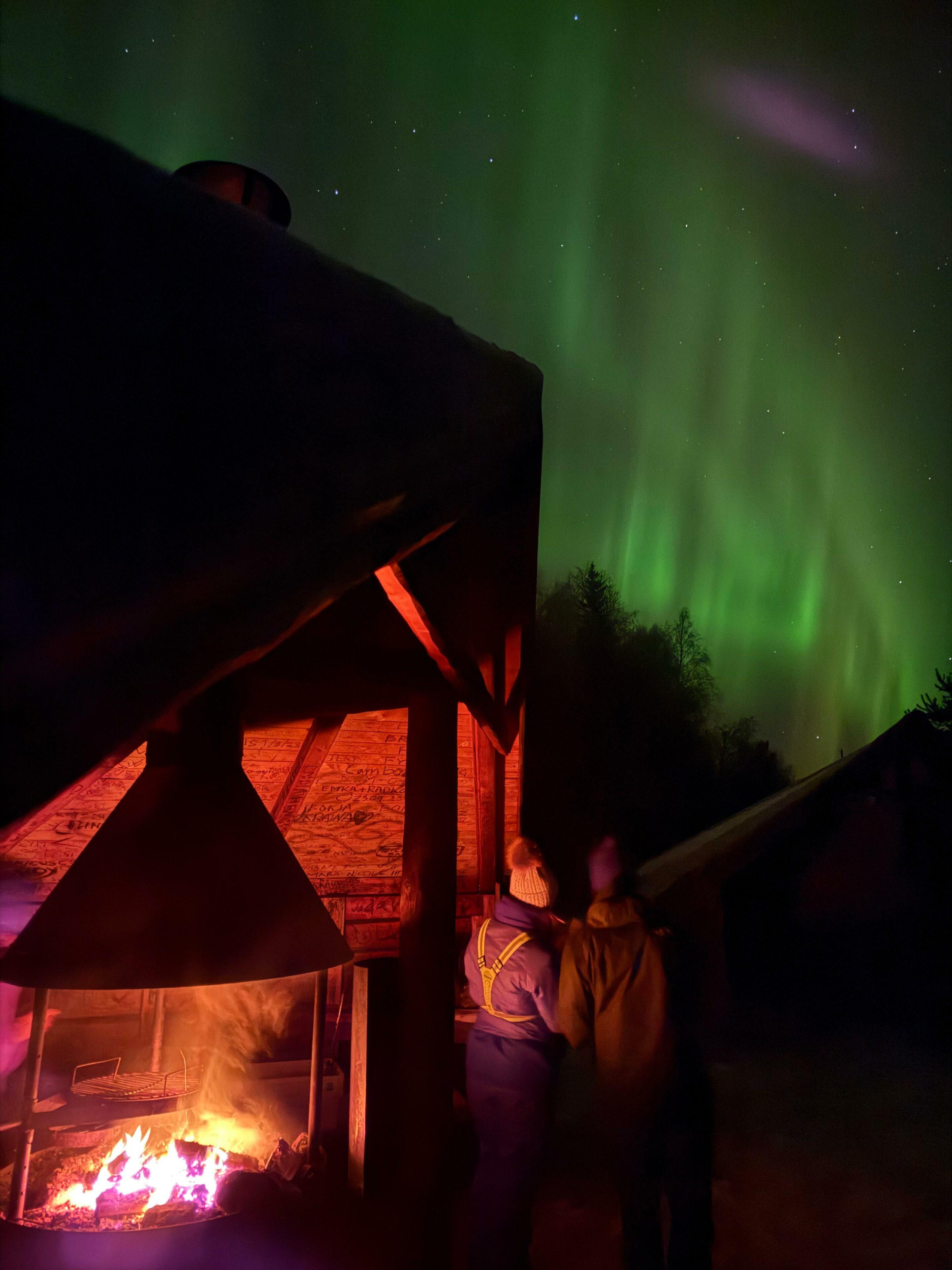 a couple watching northern lights in a leant-to shelter in winter. Lapland Royal Adventures, Rovaniemi, Lapland, Finland