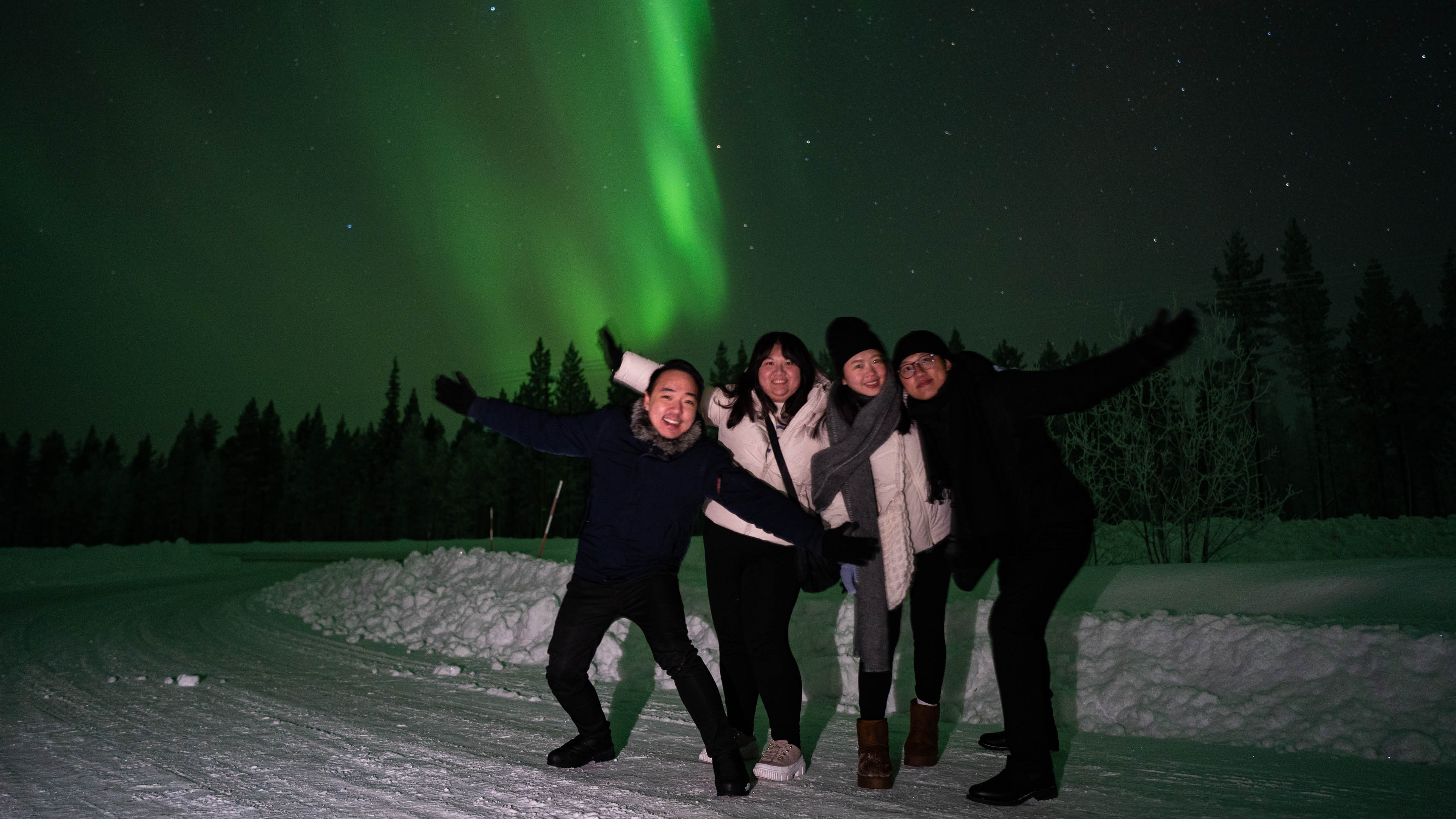 Group of people posing, behind them green northern lights in the sky. Rovaniemi, Lapland, Finland