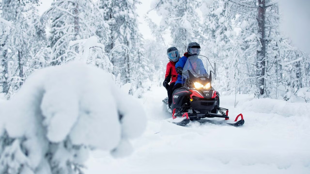 Two persons on a snowmobile in a snow covered forest in Rovaniemi, Lapland, Finland, PolarMax Adventures