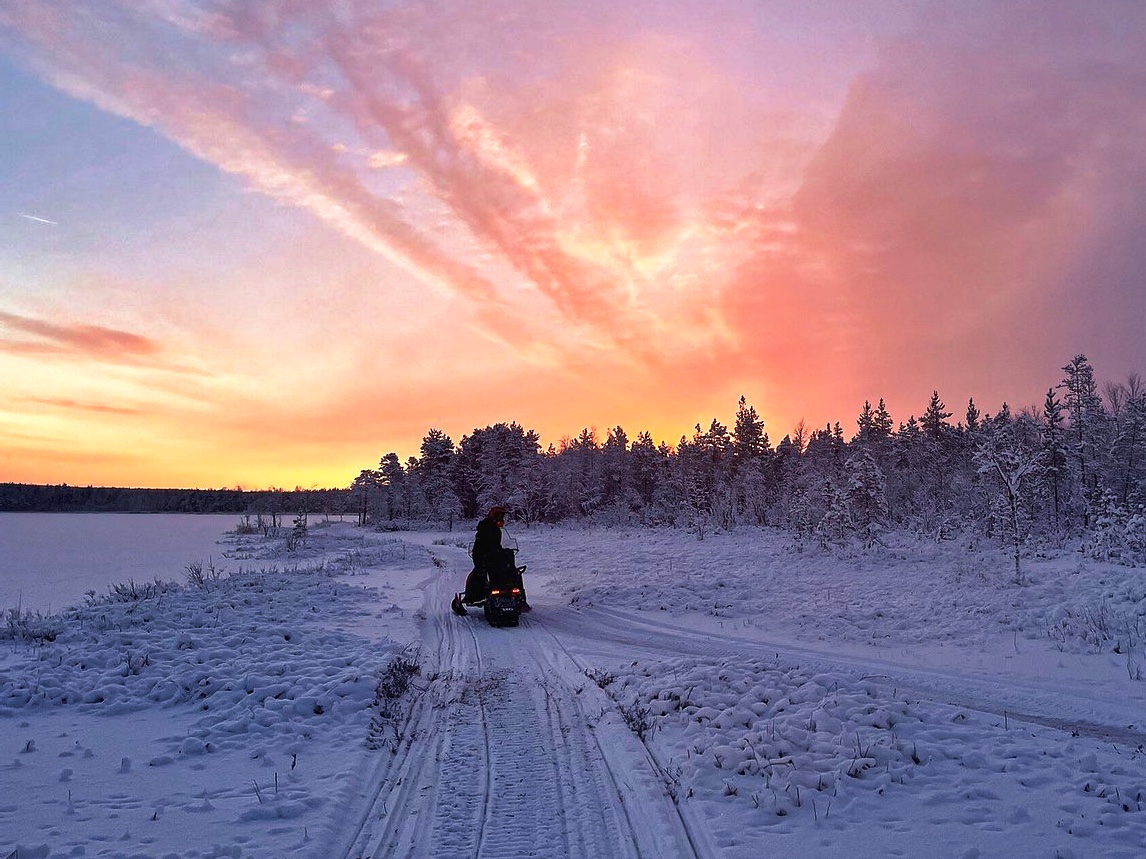 Person on a snowmobile in wintertime with a colourful sunset in the sky, Rovaniemi, Lapland, Finland, PolarMax Adventures